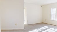 This single-floor unit offers a surprisingly functional layout across four bedrooms, one full bathroom, a kitchen, and a dedicated closet. The living areas are finished with neutral-toned carpet throughout, and multiple windows with blinds invite generous natural light, casting bright patterns across the floors and creating an open, airy atmosphere despite the compact footprint.

The spacious primary bedroom stands out as the largest room in the unit, offering ample space and access to a walk-in closet equipped with wire shelving for organized storage. The additional bedrooms are well-proportioned with carpeted floors and bright windows, one of which features a glass-paned exterior door providing direct outdoor access and added natural light.

The galley-style kitchen is efficiently designed with light wood cabinetry, dark laminate countertops, a stainless steel refrigerator and oven range, a built-in dishwasher, and a central window fitted with blinds. Light tile flooring completes the clean, functional aesthetic.

The full bathroom includes a shower-tub combination, a vanity, and a window with blinds that provides natural ventilation. Throughout the unit, crisp white walls, clean white trim, and consistent neutral tones create a bright, move-in ready environment suited for practical everyday living.