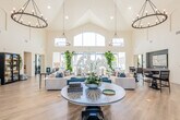 This single-story clubhouse and leasing facility combines striking architectural design with a comprehensive suite of amenities. The centerpiece is a soaring great room with a dramatic vaulted ceiling, where large pendant chandeliers hang above light hardwood flooring. Expansive floor-to-ceiling windows and an arched transom flood the space with natural light, framing views of the outdoor amenity areas. Plush seating arrangements in neutral and navy tones, accented by lush greenery, create an inviting and sophisticated atmosphere.

Adjacent to the great room, a full catering kitchen features dark shaker cabinetry, sleek charcoal countertops, a geometric tile backsplash, stainless steel appliances, and arched windows that bring in abundant natural light. A second kitchenette area offers dark cabinetry, a stylish patterned tile backsplash, and a stainless refrigerator, ideal for entertaining support.

A dedicated wet bar lounge with marble countertops, navy cabinetry, open shelving, and a decorative tile backsplash adds a refined social space. The conference room accommodates group meetings around a sleek table, bathed in light from tall arched windows. The well-appointed fitness center is equipped with a variety of strength and cardio machines, mirrored walls, and direct access to the outdoors, rounding out this thoughtfully designed community facility.