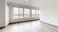 Located at 2132 Stokes Blvd in Cleveland's University Circle neighborhood, this modern single-floor unit offers a well-designed layout encompassing a combined kitchen and living area, one bedroom, two closets, a bathroom, and an in-unit laundry space. Light-toned hardwood-style flooring flows consistently throughout, lending a clean, cohesive aesthetic.

The open-concept kitchen is outfitted with grey flat-front cabinetry, black hardware, white countertops, a white subway tile backsplash, and a full suite of stainless steel appliances including a refrigerator, dishwasher, and over-the-range microwave. The adjacent living area is bright and open, benefiting from natural light.

The bedroom is a compact yet functional space highlighted by expansive floor-to-ceiling windows that frame elevated views of the Cleveland skyline and surrounding urban landscape, filling the room with abundant natural light. A louvered closet door adds a classic touch to the otherwise contemporary design.

The bathroom features a grey floating vanity with a white countertop, a large mirror, and matte black hardware and grab bar accents, maintaining the unit's modern aesthetic. The laundry area provides added convenience within the unit. Overall, the space presents a crisp, minimalist character suited to urban living.