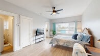 Located at 1133-1137 27th St in San Diego, CA, this efficiently designed one-bedroom, one-bathroom unit offers a thoughtfully arranged single-floor layout. The generously sized bedroom serves as the centerpiece of the space, featuring light wood-tone flooring, a ceiling fan with integrated lighting, and wide windows dressed with teal curtains that invite natural light throughout the day. The open feel of the bedroom easily accommodates a bed, dresser, desk area, and additional furnishings. A dedicated closet provides practical storage space. The galley-style kitchen is compact yet fully functional, outfitted with white shaker cabinetry, light countertops, and a gas range — making efficient use of every inch of space. Coastal-inspired artwork adorns the kitchen wall, adding a cheerful, relaxed character. The bathroom includes a classic clawfoot-style bathtub with shower, a toilet, and a window for natural ventilation. Consistent light wood flooring runs throughout, tying the space together with a clean, cohesive aesthetic. The overall ambiance is bright and airy with a coastal theme, making this unit a comfortable and practical residence in a well-established San Diego neighborhood.