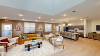 Located on Central Avenue in Chattanooga, Tennessee, this single-floor community amenity space is thoughtfully designed to offer a variety of gathering and recreational opportunities. The open-concept layout connects a welcoming lounge area to a fully equipped kitchen, creating a seamless flow ideal for social interaction.

The lounge features light wood-look flooring, recessed lighting, and tray ceiling details that add architectural dimension. Colorful artwork punctuates the warm taupe walls, while an assortment of contemporary seating — including a rich amber velvet sofa and mid-century-style accent chairs — creates an inviting atmosphere. Natural light filters through white-slatted blinds across multiple windows.

The kitchen area is anchored by a generous granite-topped island with bar seating, dark espresso cabinetry, a full-size refrigerator, and globe pendant lights suspended overhead. Adjacent to the main lounge, a secondary gathering area offers additional flexible seating with access to outdoor spaces via glass-paned doors.

A dedicated game room includes a shuffleboard table and a classic arcade cabinet, providing entertainment options for residents. A separate flexible activity room with light-filled skylights offers open floor space suitable for various uses. Together, these areas form a well-rounded, amenity-rich environment designed for community engagement.