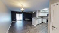 This single-floor, 1-bedroom, 1-bathroom residence offers a thoughtfully designed open-concept layout that maximizes both space and functionality. The combined living and kitchen area serves as the heart of the unit, where rich, wide-plank hardwood-style flooring flows continuously throughout, creating a cohesive and polished aesthetic.

The kitchen is outfitted with crisp white cabinetry, granite countertops, and a central island that features a built-in sink, providing both additional prep space and a natural dividing point between the kitchen and living area. A pendant light fixture above the island adds a refined touch, complementing the striking globe chandelier that anchors the living space.

The living area is characterized by deep navy accent walls that lend a bold, modern contrast to the light ceiling and flooring. A sliding glass door floods the space with natural light while offering direct access to the outdoors. A floor-level HVAC vent ensures year-round climate comfort throughout the open floor plan.

Overall, the unit presents a clean, contemporary feel with a well-balanced combination of dark and light tones, modern lighting fixtures, and functional design elements that make efficient use of every square foot.