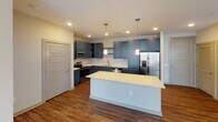 This single-floor residence offers a thoughtfully designed open-concept layout that seamlessly connects the kitchen and living area. The kitchen is a standout feature, showcasing bold slate-blue shaker-style cabinetry, light quartz countertops, a classic subway tile backsplash, and a full suite of stainless steel appliances including a range, microwave, dishwasher, and French door refrigerator with an ice maker. A spacious central island provides additional prep space and casual seating, while pendant lighting adds a polished finishing touch. Rich dark hardwood-style flooring runs throughout the kitchen and living area, which is bright and open, benefiting from multiple windows that invite natural light. The two bedrooms are generously sized, each finished with plush neutral carpet and equipped with ceiling fans. Windows fitted with blinds offer views of the surrounding building exterior while maintaining privacy. The unit includes two full bathrooms: one features a sleek vanity with navy cabinetry and a glass-enclosed walk-in shower with tiled walls, while the second offers a soaking tub and shower combination surrounded by clean white subway tile. Together, the spaces create a functional and contemporary living environment with a cohesive, modern aesthetic throughout.