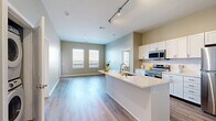 Located at 220 Vine Street in Columbus, Ohio, this well-appointed two-bedroom, two-bathroom residence offers a thoughtfully designed single-floor layout. The open-concept living and kitchen area is anchored by a large center island with a white quartz countertop and an integrated sink, complemented by white shaker-style cabinetry, a tile backsplash, and a full suite of stainless steel appliances. Track lighting overhead and multiple windows allow natural light to fill the space, which flows seamlessly onto durable wood-style flooring throughout the main areas. A dedicated pantry provides ample storage off the kitchen. Both bedrooms feature plush carpeting and generous closet space — the primary bedroom includes a spacious walk-in closet with wire shelving systems, while the second bedroom offers its own reach-in closet. The primary bathroom is finished with a double-sink vanity featuring white cabinetry and dark hardware, a large framed mirror, and a glass-enclosed shower. The second bathroom mirrors the clean aesthetic with a single-sink vanity and a full shower-tub combination. Neutral warm-toned walls throughout the home create a cohesive and inviting atmosphere.