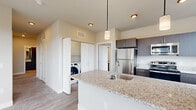 This well-appointed single-floor residence offers a thoughtfully designed layout that balances modern finishes with functional living spaces. The open-concept kitchen serves as a centerpiece, showcasing granite countertops, a large island with an undermount sink, dark espresso cabinetry, stainless steel appliances, and elegant pendant lighting. Seamlessly connected to the living area, the space flows toward expansive sliding glass doors that open to a balcony, flooding the room with natural light and offering scenic outdoor views of the surrounding neighborhood and treeline.

The bedrooms are carpeted for comfort, each equipped with ceiling fans and windows that frame pleasant outdoor vistas. Ample storage is provided through a generously sized walk-in closet fitted with wire shelving, as well as additional reach-in closets. The bathroom is finished with the same granite countertop aesthetic found in the kitchen, complemented by a dark-framed vanity mirror, a full tub-shower combination, and wood-look flooring.

A dedicated in-unit laundry area with a full-size washer and dryer adds convenience. Throughout the residence, light wood-look hard flooring ties the main living areas together, while neutral warm tones on the walls create a clean, cohesive ambiance throughout.