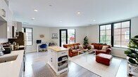 This 2-bedroom, 2-bathroom unit at 28 Gould Street in Reading, MA offers a well-designed, single-floor layout that balances modern finishes with functional living. The entryway opens to a welcoming hallway with light wood-style flooring that flows throughout the main living areas. The open-concept kitchen and living space serves as the heart of the home, featuring a sleek kitchen with high-gloss white cabinetry, subway tile backsplash, stainless steel appliances, and a freestanding island with a butcher block top for additional prep and storage. Large, black-framed windows flood the living area with natural light and offer views of the surrounding neighborhood. The spacious living room provides ample room for both lounging and dining. The primary bedroom is generously sized with large windows and plush carpeting, while the second bedroom offers flexible use as a home office or fitness space. The two bathrooms include a full bath with a soaking tub and large-format tile flooring, and a second bath with a walk-in shower and clean, neutral finishes. Recessed lighting and a neutral color palette create a bright, cohesive atmosphere throughout this thoughtfully designed residence.