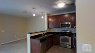 This single-floor space showcases a well-appointed kitchen that serves as a central feature of the layout. The kitchen is outfitted with rich, dark wood cabinetry that extends to the upper walls, providing generous storage throughout. Black granite countertops offer a sleek contrast against the cabinetry and run continuously across the workspace and along the breakfast peninsula, which doubles as a natural divider between the kitchen and the adjacent living area. The peninsula is equipped with a stainless steel sink and pendant lighting above, adding a refined touch to the space.

Stainless steel appliances, including a range, microwave, and dishwasher, are seamlessly integrated into the cabinetry, contributing to a cohesive, modern aesthetic. The kitchen flooring features neutral tile, while the adjacent living area transitions to carpet, helping to visually define each zone. Recessed and flush-mount ceiling fixtures provide consistent overhead lighting throughout. The open-concept design between the kitchen and living area enhances the sense of flow and connectivity, making the space feel functional and inviting.