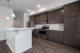 This two-story home is thoughtfully designed to maximize functionality across two floors. The main level hosts an open-concept living and kitchen area unified by warm wood-look flooring throughout. The kitchen features dark wood cabinetry with modern stainless steel appliances, a built-in microwave, pendant lighting, and a breakfast bar, while a separate kitchen unit showcases contemporary taupe cabinetry paired with white quartz countertops and an electric range. The living area benefits from abundant natural light streaming through multiple large windows and a glass-paneled entry door, complemented by a ceiling fan overhead. A staircase leads to the upper level, where four bedrooms are carpeted for comfort, each featuring large windows with outdoor views. The primary bedroom offers a generous footprint with neutral tones and soft carpeting. Two bathrooms serve the home: one featuring a walk-in glass-door shower with wood-look flooring, and another with a tub-shower combination and a window for natural light. Both bathrooms include quartz-topped vanities. A dedicated laundry area with a built-in countertop and sloped ceiling detail adds practical utility to the upper floor.