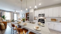 This thoughtfully designed one-bedroom, one-bathroom residence in Suwanee, GA offers a cohesive open-concept floor plan with modern finishes and a neutral color palette throughout. The kitchen serves as the centerpiece of the living space, boasting crisp white shaker cabinetry extending to the ceiling, granite countertops, stainless steel appliances including a refrigerator, range, and built-in microwave, and a spacious island with an undermount sink and pendant lighting overhead — ideal for both meal preparation and casual dining with bar seating. The kitchen flows seamlessly into the living room, which features wood-look flooring, a ceiling fan, and large windows with access to an outdoor area, filling the space with abundant natural light. A built-in shelving unit adds both storage and a warm, decorative accent between the two areas. The bedroom is a comfortable retreat with a ceiling fan, natural light from a large window, and wood-look flooring. The walk-in closet provides ample storage with wire shelving systems. The bathroom features granite countertops, white cabinetry, a large mirror, and a tub-shower combination with clean subway tile surround. Wood-look flooring ties all rooms together for a consistent, polished aesthetic.