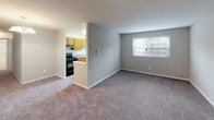 This single-floor residential unit offers a practical and comfortable layout designed for everyday living. The kitchen is equipped with warm honey-toned wood cabinetry, laminate countertops, a stainless steel sink, and a black gas range with overhead ventilation. It opens toward the living area, creating a connected flow between cooking and entertaining spaces. The living room is generously proportioned, featuring soft wall-to-wall carpeting in a neutral gray tone and a window that brings in natural light with views of the surrounding greenery. Adjacent to the living area, the dining space is highlighted by an elegant chandelier, adding a touch of classic character to the room. Multiple bedrooms carry the same neutral carpeting and soft gray wall palette, each benefiting from natural light provided by windowed walls with blinds. One bedroom features a double-door closet with a rod and shelf system, offering ample storage. The bathroom is clean and functional, presenting a full tub and shower combination with chrome fixtures, tile flooring in a neutral stone pattern, and a vanity with wood cabinetry. Throughout the unit, white trim, consistent neutral tones, and plush carpeting create a cohesive, move-in-ready atmosphere.
