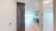 This one-bedroom, one-bathroom residence in San Diego's 92103 zip code offers a thoughtfully designed layout with modern finishes throughout. Light wood-tone flooring runs continuously across the open-concept kitchen and living area, creating a cohesive and airy feel. The kitchen features a sleek, contemporary design with flat-front cabinetry in contrasting taupe and dark tones, a tile backsplash, stainless steel appliances including a gas range and built-in microwave, and an undermount sink. Recessed lighting illuminates the space efficiently.

Floor-to-ceiling windows in the living area and bedroom frame sweeping city views, while sliding glass doors open directly onto a private balcony. A distinctive exposed concrete structural column adds an industrial architectural element to the living space. The bedroom includes a walk-in closet outfitted with built-in shelving and hanging rods, accessed via a sliding barn-style door.

The bathroom features large-format tile flooring, a floating wood-toned vanity with an integrated sink, a full-width mirror, and a frameless glass walk-in shower with tile surround. The overall design aesthetic is clean, minimalist, and contemporary throughout.