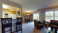 This single-floor residence offers a thoughtfully designed layout that balances functionality and comfort. The kitchen is a standout feature, showcasing rich dark cabinetry paired with light granite countertops, dark hardwood-style flooring, and a full suite of stainless steel appliances including a refrigerator, range, over-the-range microwave, and dishwasher. A structural pass-through with a built-in countertop connects the kitchen to the adjacent living area, creating an open, communicative flow between spaces. The living room is generously proportioned, featuring the same dark hardwood-style flooring, neutral warm-toned walls, a textured ceiling, and large windows with a sliding glass door that invite natural light and outdoor views. The bedrooms are carpeted in a neutral tone, offering a comfortable and quiet retreat, with one bedroom featuring a window with a closet and another with direct hallway access. The bathroom is clean and classic, with a full soaking tub and shower surrounded by white tile, a dark wood vanity with a white countertop, a large mirror, and stone-look tile flooring. Throughout the residence, a consistent neutral color palette and cohesive finishes create a polished, move-in-ready atmosphere.