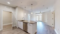 Located at 111 Grove Park Dr in Mooresville, NC, this single-floor, 3-bedroom, 2-bathroom home offers a well-designed open-concept layout with modern finishes throughout. The kitchen serves as a central hub, featuring a large island with a quartz-style countertop, undermount sink, stainless steel appliances including a refrigerator, range, microwave, and dishwasher, white cabinetry, and a classic subway tile backsplash. Pendant lighting above the island adds a polished touch. The kitchen flows seamlessly into the living area, which is bathed in natural light from French doors topped with a transom window. A ceiling fan adds comfort to this bright, open space. Hardwood-style flooring runs throughout, lending a clean and cohesive aesthetic. The primary bedroom is generously sized and also features French doors with a transom window, offering an airy feel. The primary bathroom is well-appointed with a soaking tub, separate glass-enclosed shower, white subway tile surround, a dual-sink vanity with white cabinetry, and wood-look flooring. The second bathroom includes a tub-shower combo and white vanity. A dedicated laundry room with full-size washer and dryer adds everyday convenience. Two closets and a hallway complete this thoughtfully organized home.