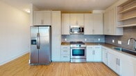 Located in the Brooklyn Village neighborhood of Charlotte, NC, this single-floor unit offers a clean, contemporary design with light wood-tone flooring running throughout the entire space, creating a cohesive and inviting atmosphere.

The kitchen is a standout feature, outfitted with white shaker-style cabinetry, a textured tile backsplash, warm countertops, and a full suite of stainless steel appliances including a side-by-side refrigerator with ice maker, gas range, over-the-range microwave, and dishwasher. Ample upper and lower cabinet storage, along with open shelving, adds both function and visual interest to the space.

The living area is open and airy, bathed in natural light from a set of French doors that open to an exterior balcony, offering views of the surrounding neighborhood. Recessed lighting complements the natural light, keeping the space bright and welcoming.

The bathroom is well-appointed with white cabinetry, a dual-sink vanity with a gray countertop, a tiled tub-shower combination, and wood-look flooring that ties seamlessly into the rest of the unit. The layout is practical and efficiently organized.

Throughout the unit, crisp white walls, clean lines, and modern hardware contribute to a polished, move-in-ready aesthetic suited for contemporary urban living in Charlotte.