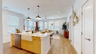 Located in San Antonio's Alamo Ranch area, this thoughtfully designed one-bedroom, one-bathroom unit offers a modern open-concept layout with warm finishes throughout. Light wood-tone flooring flows seamlessly across the entire space, complementing the crisp white walls and contemporary aesthetic.

The kitchen is a standout feature, showcasing a large center island with a farmhouse sink, white quartz countertops, warm wood cabinetry, stainless steel appliances, subway tile backsplash, and pendant lighting overhead. The island doubles as a breakfast bar with seating for multiple guests. A dedicated dining area sits just off the kitchen, bathed in natural light from a bank of large windows dressed with bold red curtains, creating a bright and inviting atmosphere.

The living area flows naturally from the kitchen and dining space, offering a comfortable, open setting complete with a ceiling fan and additional recessed lighting. The bedroom provides a well-proportioned retreat with ample natural light and a generously sized walk-in closet outfitted with built-in shelving and hanging rods on multiple walls. The bathroom features a double-sink vanity with wood cabinetry, a walk-in glass-enclosed shower with stone tile, and wood-look flooring. Additional highlights include a pantry, laundry room, and an outdoor patio.