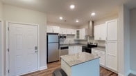 Located at 240 Pine Knot Lane in Graham, North Carolina, this single-story residence offers a clean, contemporary design with thoughtfully selected finishes throughout. The open-concept layout connects the kitchen directly to the living area, creating a cohesive and functional living space. Rich hardwood-style flooring anchors the main areas, transitioning to plush carpeting in the bedrooms.

The kitchen is a standout feature, showcasing white shaker-style cabinetry, granite countertops, and a central island that provides additional prep and seating space. A full suite of stainless steel appliances—including a refrigerator, electric range, dishwasher, microwave, and a wall-mounted range hood—equips the space for everyday use. Glass-front upper cabinets add a refined touch.

Bedrooms are carpeted and generously sized, each equipped with ceiling fans and natural light from large windows with blinds. At least one bedroom includes access to a spacious walk-in closet outfitted with wire shelving and hanging rods for organized storage.

The bathrooms feature tile flooring, tub/shower combinations with brushed nickel fixtures, and built-in wire shelving for added convenience. The overall palette of neutral tones and crisp white trim lends a fresh, move-in-ready quality to the entire home.