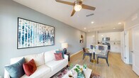 This single-floor residence offers a thoughtfully designed open-concept layout that seamlessly connects the living, dining, and kitchen areas. Light wood-style flooring flows throughout the main living spaces, complemented by soft blue-grey accent walls and recessed lighting that create a calm, contemporary ambiance. The living room is generously proportioned, featuring a ceiling fan, large windows that invite abundant natural light, and ample room for comfortable seating arrangements. Adjacent to the living area, the dining space provides an inviting setting for meals and entertaining. The kitchen is a functional centerpiece of the home, boasting a large island with a quartz countertop and undermount sink, white shaker cabinetry, a subway tile backsplash, and a full suite of stainless steel appliances including a range, microwave, dishwasher, and refrigerator. Pendant lighting above the island adds a refined touch. A dedicated in-unit laundry area with a washer and dryer is conveniently located nearby. The primary bedroom features soft carpeting, a ceiling fan, and a serene color palette, while the secondary bedroom offers natural light through window blinds. Both bathrooms are finished with white cabinetry, quartz countertops, and tile surround tub-shower combinations, delivering a clean, modern aesthetic throughout.