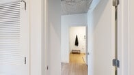 Located in Chicago's South Loop, this single-floor residence at 1400 S Wabash Ave showcases a distinctly modern industrial aesthetic defined by exposed concrete ceilings and structural columns that contrast beautifully with crisp white walls and light hardwood flooring throughout. Floor-to-ceiling windows wrap around the living areas, flooding the space with natural light while offering expansive views of the Chicago skyline and surrounding cityscape from an elevated vantage point.

The open living area is anchored by a prominent concrete column and benefits from corner-oriented windows that maximize both light and views. The galley-style kitchen features warm wood cabinetry, stainless steel appliances including a gas range, microwave, and refrigerator, along with clean white countertops that create a refined contrast to the natural wood tones.

The bedroom continues the industrial-modern aesthetic with an exposed concrete ceiling and a large picture window framing striking city views. A built-in sliding wardrobe provides streamlined storage. The bathroom is thoughtfully finished with a glass-enclosed shower clad in marble-style tile, a sleek floating vanity with an undermount sink, and wood flooring that adds warmth to the clean, minimalist design.
