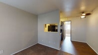 This single-floor residence offers a functional and straightforward layout connecting a living area, kitchen, bedroom, and bathroom. The living space is carpeted and features neutral walls, a ceiling fan with integrated lighting, and a pass-through window that visually connects it to the kitchen. This open design element allows light and sight lines to flow between the two areas while maintaining a defined separation.

The kitchen is designed as a galley-style space featuring gray cabinetry with brushed hardware, white countertops, a stainless steel sink, and black appliances including a refrigerator, electric range, and dishwasher. Wood-look flooring runs through the kitchen and into the hallway, adding warmth and contrast against the cabinetry.

The bedroom is carpeted and benefits from natural light provided by a window with horizontal blinds. A sliding glass patio door in an adjoining room offers additional outdoor access and natural light. The bathroom features a gray vanity with a white countertop, a large mirror, and wood-look flooring that coordinates with the rest of the unit. A programmable thermostat is conveniently located just outside the bathroom.