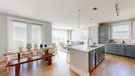 Located in Charlotte's 28277 zip code, this well-appointed 2-bedroom, 2-bathroom residence delivers a thoughtfully designed single-floor layout that balances open communal spaces with comfortable private retreats. The open-concept living, dining, and kitchen area forms the heart of the home, anchored by warm light wood flooring that flows throughout. The kitchen features two-tone cabinetry in soft gray and white, a large central island with a quartz countertop and undermount sink, stainless steel appliances, and pendant lighting — ideal for both daily cooking and entertaining. The living room is bathed in natural light from floor-to-ceiling windows and a sliding glass door, creating a bright, airy ambiance. A charming arched doorway connects the main living area to the hallway, which leads to a built-in shelving nook adding both function and character. The spacious primary bedroom includes a well-organized walk-in closet with built-in shelving and drawers. The primary bathroom offers a double-sink vanity with gray countertops, white cabinetry, and a tiled walk-in shower. The secondary bedroom features a ceiling fan and a large window with outdoor views. Both bedrooms are calm and restful in tone, complementing the home's clean, neutral palette throughout.