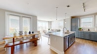 Located in Charlotte's 28277 zip code, this well-appointed 2-bedroom, 2-bathroom residence delivers a thoughtfully designed single-floor layout that balances open communal spaces with comfortable private retreats. The open-concept living, dining, and kitchen area forms the heart of the home, anchored by warm light wood flooring that flows throughout. The kitchen features two-tone cabinetry in soft gray and white, a large central island with a quartz countertop and undermount sink, stainless steel appliances, and pendant lighting — ideal for both daily cooking and entertaining. The living room is bathed in natural light from floor-to-ceiling windows and a sliding glass door, creating a bright, airy ambiance. A charming arched doorway connects the main living area to the hallway, which leads to a built-in shelving nook adding both function and character. The spacious primary bedroom includes a well-organized walk-in closet with built-in shelving and drawers. The primary bathroom offers a double-sink vanity with gray countertops, white cabinetry, and a tiled walk-in shower. The secondary bedroom features a ceiling fan and a large window with outdoor views. Both bedrooms are calm and restful in tone, complementing the home's clean, neutral palette throughout.
