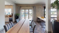 This single-floor game room is thoughtfully designed to accommodate a variety of social and recreational activities. The space is anchored by polished concrete floors throughout, lending an industrial yet refined aesthetic that ties the various zones together cohesively.

The entertainment area features a classic arcade machine and high-top tables paired with upholstered bar chairs, complemented by a trio of bold, colorful abstract artworks mounted on the wall. A full-length shuffleboard table sits beneath a wall-mounted flat-screen television, providing a focal point for friendly competition.

A built-in banquette dining nook offers a more intimate setting, with a navy leather bench seat, wood-framed tables, and striped accent chairs arranged beneath a series of sleek pendant lights. A textured feature wall adds visual depth to this seating alcove.

The dining area extends toward a set of French doors framed by patterned drapes, opening to views of an outdoor pool. A mosaic-tiled accent wall adds warmth and texture, while a long bar-height counter with stools provides additional seating. Natural light flows in generously through the glass doors, enhancing the welcoming ambiance of the space.