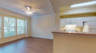 This single-floor, 1-bedroom, 1-bathroom unit offers a practical and well-organized layout designed for comfortable everyday living. The open-concept living area features warm hardwood-style flooring, a ceiling fan with light fixture, and a large window that invites abundant natural light and outdoor views. Crown molding and a textured ceiling add subtle architectural character to the space.

The kitchen flows seamlessly from the living area, separated by a raised breakfast bar with a laminate countertop. White cabinetry provides ample storage, and the kitchen is equipped with a white electric coil range and an exhaust hood above. A window in the kitchen further brightens the cooking space.

The bedroom is generously sized with plush carpeting, a ceiling fan, and a window fitted with blinds for privacy and light control. The room offers ample wall space and a calm, neutral atmosphere.

The bathroom is cleanly appointed with a wide vanity featuring white cabinetry and a single sink, a tub-shower combination with tiled surround, and hardwood-style flooring. A separate water closet door provides additional privacy. The overall color palette throughout the unit is warm and neutral, creating a cohesive and inviting ambiance.