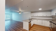 This well-designed single-floor unit offers a bright and functional layout that seamlessly connects the kitchen and living areas. The open-concept kitchen is a standout feature, equipped with stainless steel appliances including a refrigerator and range, a peninsula island with an integrated sink and dishwasher, and an abundance of white flat-panel cabinetry with ample counter space. Recessed lighting and a ceiling fan overhead contribute to a clean, contemporary aesthetic throughout the main living area, which is finished with warm wood-style flooring that extends across the open floor plan.

The living space is generously proportioned, filled with natural light from large windows fitted with blinds, and leads to carpeted bedroom areas that offer a softer, quieter environment. The bedrooms are simply designed with neutral walls, baseboard heating, and additional windows that allow for outside views and natural illumination.

Throughout the unit, the consistent use of neutral tones — crisp whites, soft grays, and warm wood hues — creates a cohesive and inviting ambiance. The layout is practical and well-organized, with clear transitions between living, dining, kitchen, and sleeping zones, making this space both comfortable and highly functional for everyday living.