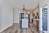 This modern single-floor residence in Atlanta, Georgia, showcases a thoughtfully designed open layout with high-quality finishes throughout. The kitchen serves as a central highlight, featuring light wood cabinetry with matte black hardware, a gray subway tile backsplash, white quartz countertops, and a full suite of stainless steel appliances including a gas range, over-the-range microwave, refrigerator, and dishwasher. A large kitchen island with a white quartz surface provides additional workspace and flows seamlessly into the main living area, which features warm wood-look plank flooring and pendant lighting overhead. The bedrooms offer plush carpeting, ceiling fans, and tall windows that invite natural light and views of the surrounding Atlanta cityscape. The primary bedroom connects directly to an en-suite bathroom appointed with a dual-sink vanity, wood-toned cabinetry, matte black fixtures, a glass-enclosed walk-in shower, and a separate soaking tub. A secondary bathroom mirrors the refined aesthetic with a tiled tub-surround, wood vanity, and wood-look flooring. Bold paneled doors and clean white walls complete the contemporary character of this well-appointed Atlanta residence.