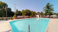 Located at 7999 Wildflower Ln in Westerville, Ohio, this single-level outdoor recreational facility centers around a generously sized swimming pool with crystal-clear blue water. The pool area is thoughtfully designed for leisure and relaxation, offering an expansive pool deck lined with rows of lounge chairs and chaise seating, ideal for sunbathing and poolside gatherings. A charming gazebo-style pool house anchors one side of the facility, providing shade and a convenient service or storage structure. The grounds are enclosed by a perimeter fence, ensuring privacy and security, while mature trees lining the boundary create a lush, natural backdrop that enhances the serene outdoor atmosphere. Decorative potted plants add greenery and visual interest throughout the deck area. The open-air setting benefits from abundant natural sunlight, making it a welcoming destination during warm weather. An American flag proudly flies on a flagpole within the facility, adding a classic community feel. Overall, this well-appointed outdoor pool facility offers a comfortable and inviting environment suited for community recreation and relaxation in the heart of Westerville, Ohio.