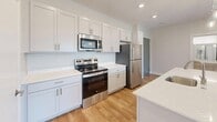 This contemporary apartment in Blubell, Omaha, offers 1070 square feet of thoughtfully designed living space. The single-floor layout comprises two bedrooms, two bathrooms, and an open-concept kitchen and living area. The primary bedroom is generously sized at 140 square feet, providing ample space for comfort.

The interior is characterized by its bright, airy ambiance, achieved through large windows that flood the rooms with natural light. The flooring alternates between warm hardwood in the main living areas and plush carpeting in the bedrooms, adding texture and comfort to the space.

The kitchen is a highlight, featuring modern white cabinetry, stainless steel appliances, and a central island with a sink, perfect for food preparation or casual dining. Pendant lighting adds a touch of elegance to this functional space.

Both bathrooms are well-appointed, with one showcasing a spacious walk-in shower. The apartment also includes two closets for ample storage. A notable feature is the outdoor balcony, accessible through a glass door, offering views of the surrounding area and extending the living space.

The apartment's neutral color palette and clean lines create a canvas for personal style, while ceiling fans in the bedrooms provide additional comfort. This well-designed space combines functionality with modern aesthetics, making it an ideal home in the heart of Omaha.