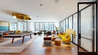 This expansive single-floor lounge spans a generous footprint and is designed with a cohesive mid-century modern aesthetic that balances social and functional zones throughout. Warm hardwood flooring runs continuously across the entire space, complemented by rich wood-paneled ceilings in select areas that add depth and a refined warmth to the interior.

The layout is thoughtfully organized into several distinct areas. A games zone features a full-size pool table and shuffleboard beneath a dramatic oversized brass drum pendant light, alongside a sleek wet bar with tiled backsplash, wall-mounted television, and counter seating. A lounge area showcases curved sofas, bold yellow accent chairs, and curated mid-century furnishings arranged around layered area rugs, bathed in natural light from floor-to-ceiling windows that frame sweeping urban skyline views.

A formal meeting or dining area includes a large conference-style table beneath a sculptural globe chandelier, topped by a warm wood ceiling and bordered by glass-partition walls. Private booths with leather banquette seating offer more intimate settings along a corridor flanked by steel-framed glass partitions. Artistic wallcovering with graphic line-art motifs punctuates the entry corridor, adding a playful, curated character. The overall ambiance is stylish, inviting, and well-appointed throughout.