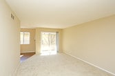 This single-floor residence offers a well-organized layout with a cohesive neutral color palette of warm beige tones throughout. The living area features hardwood-style flooring and a ceiling fan, with natural light streaming in through a sliding glass door that opens to an outdoor view, adding a sense of openness to the space.

Adjacent to the living area, the galley-style kitchen is efficiently designed with white cabinetry, granite-look countertops, a stainless steel sink, and white appliances including a coil-burner range and full-size refrigerator. Hardwood-style flooring continues through the kitchen, complementing the clean, functional aesthetic.

The bedrooms are carpeted and finished with the same warm neutral walls. Each room features windows that admit natural light and views of the surrounding exterior. The layout, as visible in the 3D model, places the bedrooms toward one end of the unit, providing a clear separation from the living spaces.

Two bathrooms serve the unit, each featuring tile flooring, white vanity cabinetry with granite-look countertops, large mirrors, and chrome fixtures. One bathroom includes a bathtub. Both bathrooms maintain a clean, consistent style that aligns with the overall design of the space.