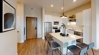 Located at 213 14th Ave SW in Rochester, Minnesota, this contemporary residential unit offers a thoughtfully designed, single-floor layout with a seamless blend of modern finishes and functional living spaces. The open-concept kitchen and living area serves as the heart of the home, featuring white shaker cabinetry, a subway tile backsplash, stainless steel appliances, and a central island with bar seating — ideal for both everyday meals and casual entertaining. Light wood-style flooring runs throughout the main living areas, adding warmth and continuity. The living room is anchored by large floor-to-ceiling windows and a glass door that opens to a private balcony, offering sweeping views of the surrounding Rochester landscape and filling the space with abundant natural light. The unit includes two well-proportioned bedrooms, each with plush carpeting and generous window views. Exposed concrete architectural columns in the primary bedroom add an industrial design accent. The bathrooms are finished with clean white vanities and ample built-in storage, and a walk-in closet connects directly to one of the bathrooms for added convenience. Recessed lighting and pendant fixtures throughout enhance the modern, refined ambiance of this well-appointed space.