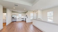 This two-story unit offers a thoughtfully designed layout spread across two levels, with the main living spaces occupying the upper floor and an attached garage with staircase access on the ground level. The garage provides a clean, bright space with a concrete floor and overhead fluorescent lighting, offering convenient storage or parking.

Ascending to the main level, the open-concept living area greets you with warm wood-look flooring, crisp white walls, and abundant natural light streaming through multiple windows. A tray ceiling with a ceiling fan adds architectural interest to the living space, enhancing the sense of height and airflow.

The kitchen is a standout feature, outfitted with white shaker-style cabinetry reaching toward the ceiling, light quartz countertops, a classic subway tile backsplash, and a full suite of stainless steel appliances including a French door refrigerator, electric range, over-the-range microwave, and dishwasher. A stainless farmhouse sink adds a refined, practical touch.

The spacious bedroom features wood-look flooring, a ceiling fan, and a window with outdoor views, while a dedicated closet provides ample storage. The full bathroom is finished with large-format white tile in the tub/shower surround, wood-look flooring, brushed gold fixtures, and a white vanity with a clean countertop surface.