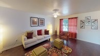 This two-story residence offers a well-organized layout with distinct living spaces across both levels. The kitchen is equipped with warm oak cabinetry extending to the ceiling, a double stainless steel sink, white appliances including an electric range and refrigerator, light countertops, and durable dark flooring. A pass-through window connects the kitchen directly to the living area, enhancing the open feel between spaces.

The living room features dark hardwood-style flooring, a ceiling fan with light fixture, and a window dressed in red curtains that allows natural light to flow in. The space flows into a dedicated dining area, which includes a window overlooking a green outdoor view and convenient closet storage nearby.

The bedrooms are carpeted and vary in size, with one featuring vaulted ceilings and another offering a bright window with neutral curtains. Both bathrooms include a full tub and shower combination. One bathroom features a single vanity with integrated sink, while the second is finished in a similarly practical style.

Throughout the home, textured ceilings, neutral walls, and consistent flooring create a cohesive and functional living environment across both floors.