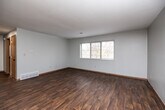 Located at 1958 Broadway St in Iowa City, Iowa, this 2-bedroom, 1-bathroom single-floor unit offers a functional and straightforward layout. The living room is an open, well-lit space featuring rich, dark hardwood-style flooring, neutral gray walls, and a ceiling fan. Large windows allow natural light to pour in, offering views of surrounding trees that lend a sense of privacy and nature. The galley-style kitchen is efficiently designed with warm oak cabinetry lining both walls, light-colored countertops, a double-basin sink, and black appliances including a refrigerator and range, complemented by matching hardwood-style flooring. Both bedrooms are carpeted for comfort and feature neutral tones. The primary bedroom is a well-proportioned space with a wide window framing outdoor greenery and a dedicated closet with a hanging rod. The second bedroom also includes a closet and connects easily to the main hallway. The full bathroom is clean and practical, equipped with a tub and shower combo, toilet, and a vanity with cabinet storage. Wood-toned interior doors and warm baseboards throughout tie the space together with a cohesive, understated aesthetic.