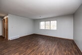 Located at 1958 Broadway St in Iowa City, Iowa, this 2-bedroom, 1-bathroom single-floor unit offers a functional and straightforward layout. The living room is an open, well-lit space featuring rich, dark hardwood-style flooring, neutral gray walls, and a ceiling fan. Large windows allow natural light to pour in, offering views of surrounding trees that lend a sense of privacy and nature. The galley-style kitchen is efficiently designed with warm oak cabinetry lining both walls, light-colored countertops, a double-basin sink, and black appliances including a refrigerator and range, complemented by matching hardwood-style flooring. Both bedrooms are carpeted for comfort and feature neutral tones. The primary bedroom is a well-proportioned space with a wide window framing outdoor greenery and a dedicated closet with a hanging rod. The second bedroom also includes a closet and connects easily to the main hallway. The full bathroom is clean and practical, equipped with a tub and shower combo, toilet, and a vanity with cabinet storage. Wood-toned interior doors and warm baseboards throughout tie the space together with a cohesive, understated aesthetic.