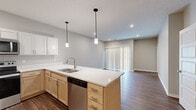 This well-appointed single-floor residence offers a thoughtfully designed open-concept layout that seamlessly connects the kitchen and living areas. The kitchen serves as the heart of the home, featuring a large central island with white quartz countertops, a stainless steel sink, and pendant lighting overhead. Light wood cabinetry along the lower level is paired with crisp white upper cabinets, creating a clean, two-tone aesthetic. A full suite of stainless steel appliances — including a refrigerator, range, microwave, and dishwasher — adds a contemporary, functional touch. Rich wood-look flooring runs throughout the entire space, lending warmth and continuity to every room. The living area is bathed in natural light through a large sliding glass door dressed with vertical blinds. The bedrooms are generously sized, each featuring ceiling fans and walk-in or reach-in closets with built-in shelving for ample storage. One bedroom benefits from a dedicated walk-in closet with an adjoining laundry area, adding everyday convenience. Neutral gray walls and white trim throughout create a bright, modern palette, while recessed lighting and well-placed fixtures ensure a consistently well-lit environment. The overall ambiance is clean, contemporary, and move-in ready.