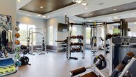 Located at 3585 SW 38th Terrace in Ocala, Florida, this expansive fitness center is a comprehensively outfitted facility designed to support a wide range of workout disciplines. The space is organized into several distinct training zones across a single floor, each thoughtfully appointed with professional-grade equipment and modern finishes.

The cardio zone features a full lineup of treadmills, stationary bikes, spin cycles, stair climbers, and rowing machines, positioned alongside large windows that invite natural light and offer pleasant views of the surrounding greenery. A dedicated strength training area houses cable machines, multi-functional rig systems, and an extensive dumbbell rack, complemented by floor-to-ceiling mirrors that enhance the sense of space.

A functional training zone provides ample open floor space, medicine ball racks, resistance bands, and TRX suspension systems, while a boxing area includes a heavy punching bag and speed bag station. Wall-mounted TVs are positioned throughout for entertainment and interactive workout programming.

Architectural details include coffered ceilings with warm wood inlays, recessed lighting, and contemporary pendant fixtures that elevate the aesthetic. Durable wood-look flooring runs throughout, and a tiled water station with dual fountains serves practical hydration needs. The facility's open layout and abundant natural light create an energizing and welcoming environment suited for all fitness levels.