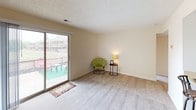 This single-floor residence at Carlton Apartments offers a practical and comfortable layout designed for everyday living. The living area is generously sized, featuring light-toned carpet, soft neutral walls, and a textured ceiling. A full-width sliding glass door floods the space with natural light and provides direct access to an outdoor patio, offering views of the surrounding community. The kitchen is efficiently arranged with white cabinetry featuring dark trim accents, a full suite of appliances including a refrigerator, electric range, built-in microwave, and dishwasher, complemented by a double-basin sink and tile flooring. An adjacent closet provides additional storage convenience. The bedroom is a quiet, carpeted retreat with warm neutral tones and a wide sliding-door closet outfitted with hanging rods and shelving, offering ample storage space. The bathroom features an extended vanity with generous counter space and a large mirror, providing ample room for daily routines. The tile flooring carries through from the bathroom into connected areas, adding a cohesive design element. Throughout the unit, the clean, light color palette and consistent finishes create a calm and welcoming ambiance suited to comfortable day-to-day living.