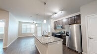 This 2-bedroom, 2-bathroom residence offers a thoughtfully designed single-floor layout that maximizes both comfort and functionality. The open-concept kitchen and living area serves as the heart of the home, anchored by a large granite-topped island with an integrated sink and pendant lighting overhead. The kitchen is outfitted with dark espresso cabinetry, stainless steel appliances including a range, microwave, refrigerator, and dishwasher, complemented by granite countertops and track lighting. Wood-look flooring runs consistently throughout the space, adding warmth and cohesion. The living area receives ample natural light through large windows fitted with horizontal blinds, and a ceiling fan provides year-round comfort. A private entry door with a sidelite window connects the space to the exterior. The primary bedroom is a comfortable retreat with a ceiling fan and its own en-suite bathroom, which features a dual-sink vanity with granite countertops, dark cabinetry, wood-look tile flooring, and a tiled shower-tub combo. The second bathroom mirrors the same quality finishes. Both bedrooms are served by dedicated closets with wire shelving systems, providing practical storage solutions. Neutral wall tones and clean white trim complete the polished, move-in-ready aesthetic throughout.