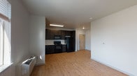 This single-floor residential unit offers a practical and well-appointed layout designed for comfortable everyday living. The open-concept kitchen and living area forms the heart of the space, featuring warm light wood-tone flooring throughout. The kitchen is equipped with dark espresso-stained cabinetry that extends to the ceiling, providing generous storage, complemented by white countertops, a subway tile backsplash, and a full suite of black appliances including a refrigerator, electric range, and over-the-range microwave. A stainless steel sink completes the functional workspace.

The bedrooms are carpeted and bathed in natural light from large windows, with baseboard and wall-unit heating systems offering climate control. Each bedroom provides a clean, neutral palette with ample space for furnishings.

The unit includes two bathrooms: one featuring a full tub-shower combo with built-in shelving and brushed nickel fixtures, and a second designed with accessibility in mind, offering a roll-in shower with grab bars, a fold-down bench, and a dark-cabineted vanity with a large mirror. Both bathrooms continue the light wood-tone flooring found throughout the main living areas, maintaining a cohesive aesthetic across the entire unit.