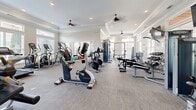 Located at 1709 Cason in Murfreesboro, Tennessee, this single-floor fitness and recreation facility offers a thoughtfully designed space for both exercise and family activity. The interior is finished with a light, neutral color palette, crown molding, and tray ceilings that lend an upscale feel to the environment. Recessed lighting and multiple ceiling fans with integrated light fixtures ensure the space remains bright and comfortable throughout.

The main fitness area is generously sized, accommodating an impressive array of cardio equipment including treadmills, ellipticals, stationary bikes, and recumbent cycles. A full wall of mirrors amplifies the sense of openness while allowing users to monitor their form. Strength training is well-represented with cable and multi-use weight machines, a dedicated dumbbell rack, and adjustable benches. Wall-mounted flat-screen televisions are strategically positioned for entertainment during workouts.

Large windows fitted with horizontal blinds line the walls, flooding the space with natural light and offering views of the surrounding exterior. A separate children's play area features soft carpet tiles, a teepee tent, foam play mats, a mini basketball hoop, and colorful toys, making this facility accommodating for families. Glass entry doors and an emergency exit ensure easy access and safety throughout the space.