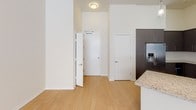 Located at 1980 Kettner Blvd, Unit #104 in San Diego, this single-floor residence offers a clean, contemporary design throughout. Light bamboo-style hardwood flooring flows through the entryway, living area, and kitchen, creating a warm and cohesive aesthetic.

The kitchen is a standout feature, outfitted with rich dark-toned cabinetry extending to the ceiling for ample storage, granite countertops, and a full suite of stainless steel appliances including a gas range, over-the-range microwave, refrigerator with in-door ice and water, and a wine cooler. The open layout connects seamlessly to the living area, which benefits from elevated ceilings and a ceiling fan overhead.

The bedroom is carpeted for comfort and features a spacious walk-in closet with built-in shelving and hanging rods. The bathroom is well-appointed with a soaking tub and shower combination, fully tiled surround, a curved shower rod, and a dark-framed recessed medicine cabinet, all complemented by tile flooring. The unit's neutral palette of crisp white walls and warm wood tones throughout lends a bright, move-in-ready feel suited to urban San Diego living.