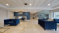 Located in Hartford, CT, this contemporary building lobby presents a polished and professional environment designed to impress. The main reception area is anchored by a bold, geometric reception desk set against a deep navy blue accent wall, complemented by a cascading crystal chandelier that adds a touch of elegance. Underfoot, large-format polished cream tiles reflect the recessed lighting above, enhancing the sense of openness throughout the space. Plush navy blue tufted sofas are thoughtfully positioned to create comfortable seating areas for visitors.

A glass-walled office suite adjacent to the main lobby offers a transparent workspace flooded with natural light from expansive street-facing windows, providing clear views of the surrounding Hartford streetscape. Nearby, a glass-enclosed lounge area features a casual seating arrangement with bar-height chairs and tables, also benefiting from generous natural light and city views.

A dedicated sitting lounge within the lobby showcases a linear fireplace framed by a dramatic veined stone surround, paired with patterned wingback chairs and a sleek glass coffee table, creating an inviting retreat. The elevator corridor features dark mosaic tile accent walls contrasted against the light flooring, maintaining the building's cohesive design language throughout. Overall, the space exudes a modern, upscale ambiance suited to a professional or residential building.