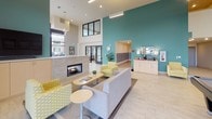 Located at 4051 S 144th St in Tukwila, Washington, this single-floor community space is thoughtfully designed to foster comfort and social interaction. The layout flows openly between distinct functional zones, unified by light wood-look flooring, neutral tones, and soaring ceilings that lend an airy, expansive feel throughout.

The central lounge area serves as the heart of the space, anchored by a sleek gas fireplace set against a tile surround. Bold teal accent walls provide striking contrast to the crisp white surroundings, while modern pendant and recessed lighting complement the abundant natural light streaming through large, floor-to-ceiling windows that frame views of the surrounding streetscape.

Seating throughout includes a mix of plush sofas, patterned accent chairs, and casual lounge benches, creating versatile arrangements suited for both relaxed socializing and quiet moments. A dedicated game area features a full-size pool table beneath tall, open ceilings adorned with framed artwork. Nearby, a café-style counter offers a small appliance station for resident convenience.

A mailbox alcove and additional seating nooks with café tables round out the amenities. A charming popcorn machine adds a playful, welcoming touch near the sun-drenched window seating area, reinforcing the inviting and community-oriented ambiance of this well-appointed space.