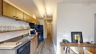 Located at 7227 N Philadelphia Ave in Portland, Oregon, this thoughtfully designed one-bedroom, one-bathroom unit offers a smart and functional single-floor layout. Hardwood-style flooring flows throughout, creating a cohesive and clean aesthetic from entry to bedroom.

The entrance leads into a well-organized corridor that connects all areas of the unit. The galley-style kitchen and living room share an open layout, with the kitchen featuring warm wood cabinetry, dark countertops, a full suite of black appliances including a range, dishwasher, refrigerator, and microwave, plus an open display shelf and stainless steel sink. Track lighting illuminates the kitchen efficiently. The adjacent living area provides a comfortable space for everyday use.

The bedroom is a cozy, well-proportioned room equipped with a ceiling fan and light fixture. Neutral walls and adequate space allow for practical furniture arrangement, and a dedicated closet adds essential storage.

The bathroom is finished with a wood-toned vanity, dark stone-style countertop, a large mirror, and a shower/tub combination. Concrete-style flooring and grab bars lend a clean, functional character to the space.

A dedicated laundry area rounds out the unit's practical amenities, making this a fully self-contained residence in Portland's St. Johns neighborhood.