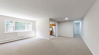Located at 835 Blooming Grove Tpke in New Windsor, NY, this two-bedroom, one-bathroom residence offers a well-organized single-floor layout designed for comfortable everyday living. The expansive living area is carpeted and bathed in natural light through large windows that frame views of surrounding greenery, with baseboard heating running along the walls. The space flows directly into a functional kitchen, which features warm honey-toned wood cabinetry, light countertops, stainless steel appliances including a refrigerator and electric range, a double sink beneath a window, and light hardwood-style flooring. The primary bedroom is generously sized, offering ample room for furnishings, and includes a sliding-door closet and neutral carpet flooring. The second bedroom is similarly appointed with carpet, a bright window, and baseboard heating. A hallway connects the private areas of the home. The full bathroom is clean and bright, featuring a tiled shower-tub combination with built-in shelving, a window for natural light, and white fixtures throughout. Neutral tones, white trim, and consistent finishes lend a cohesive and move-in-ready feel to the entire residence.