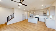 Located at 5725 S Trailside Cir W in Springfield, MO, this well-designed two-story home offers four bedrooms, three bathrooms, and a thoughtful layout spread across two evenly sized floors. The main level centers on an open-concept kitchen and living area finished with light hardwood flooring throughout. The kitchen is appointed with soft gray shaker-style cabinetry, white quartz countertops, a central island, stainless steel appliances, a decorative tile backsplash, and gold-accented hardware and faucets. Pendant lighting and recessed fixtures illuminate the space, while a ceiling fan serves the adjoining living area. The attached garage features a clean concrete floor and direct interior access. Upstairs, the four bedrooms include a generously sized primary suite, with additional bedrooms offering carpet flooring, ceiling fans, and natural light through tall windows with exterior views. The bathrooms feature distinctive touches, including botanical-print wallpaper in one water closet. Five closets—including walk-in storage with wire shelving—provide ample organization throughout. A dedicated laundry room houses a stacked washer and dryer. The home's neutral palette, modern finishes, and functional floor plan create a cohesive and inviting living environment.